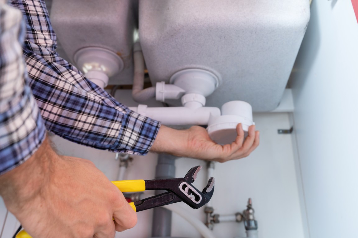 Young,Plumber,Working,With,Pipe,Wrench,In,Kitchen