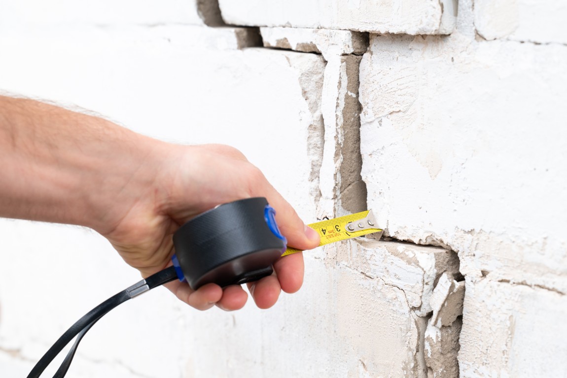 Man,Measuring,Crack,With,A,Tape,Measure.,Building,Needs,Repairing,